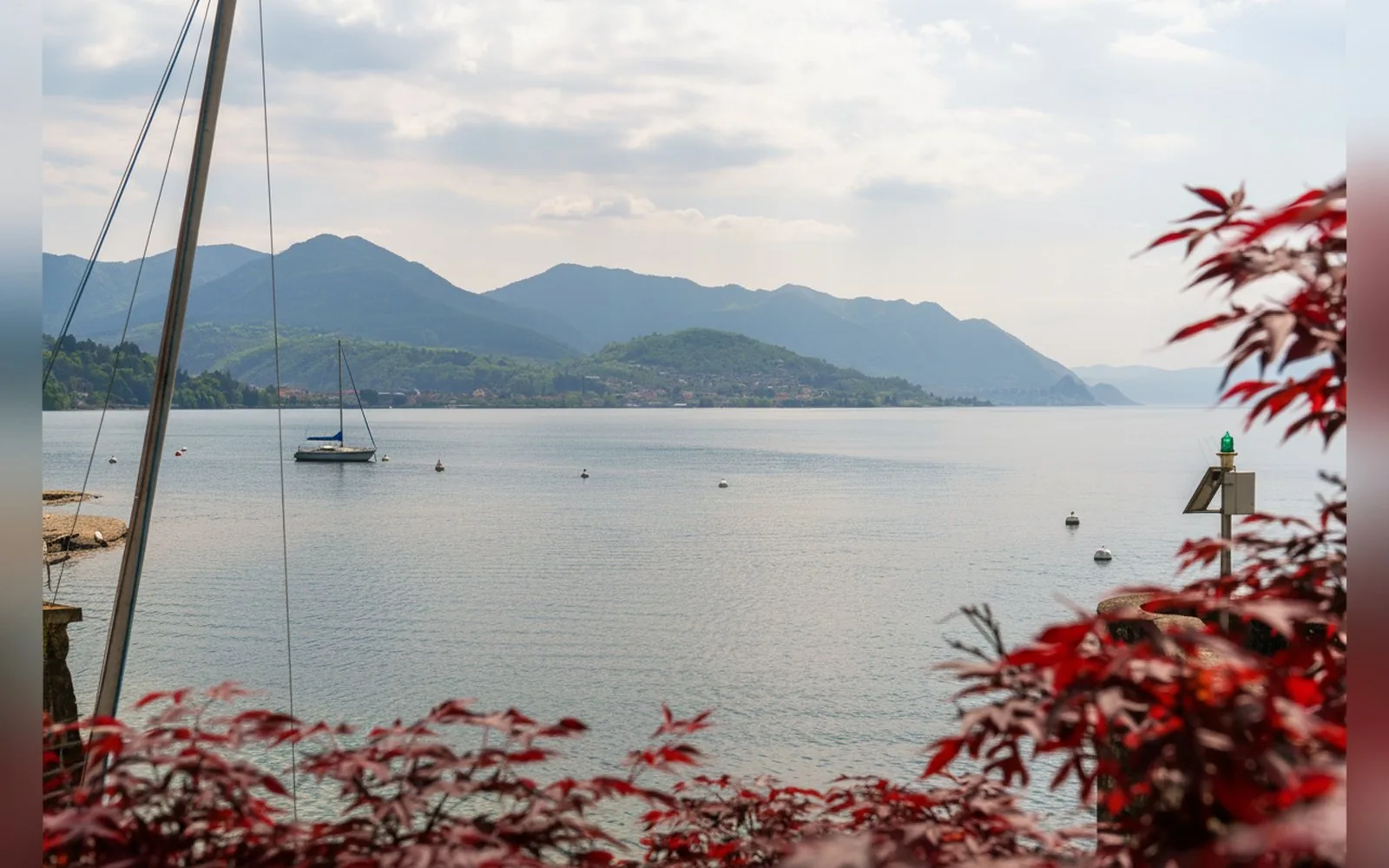 Una barca a vela sul lago inquadrata fra le foglie rosse di un acero